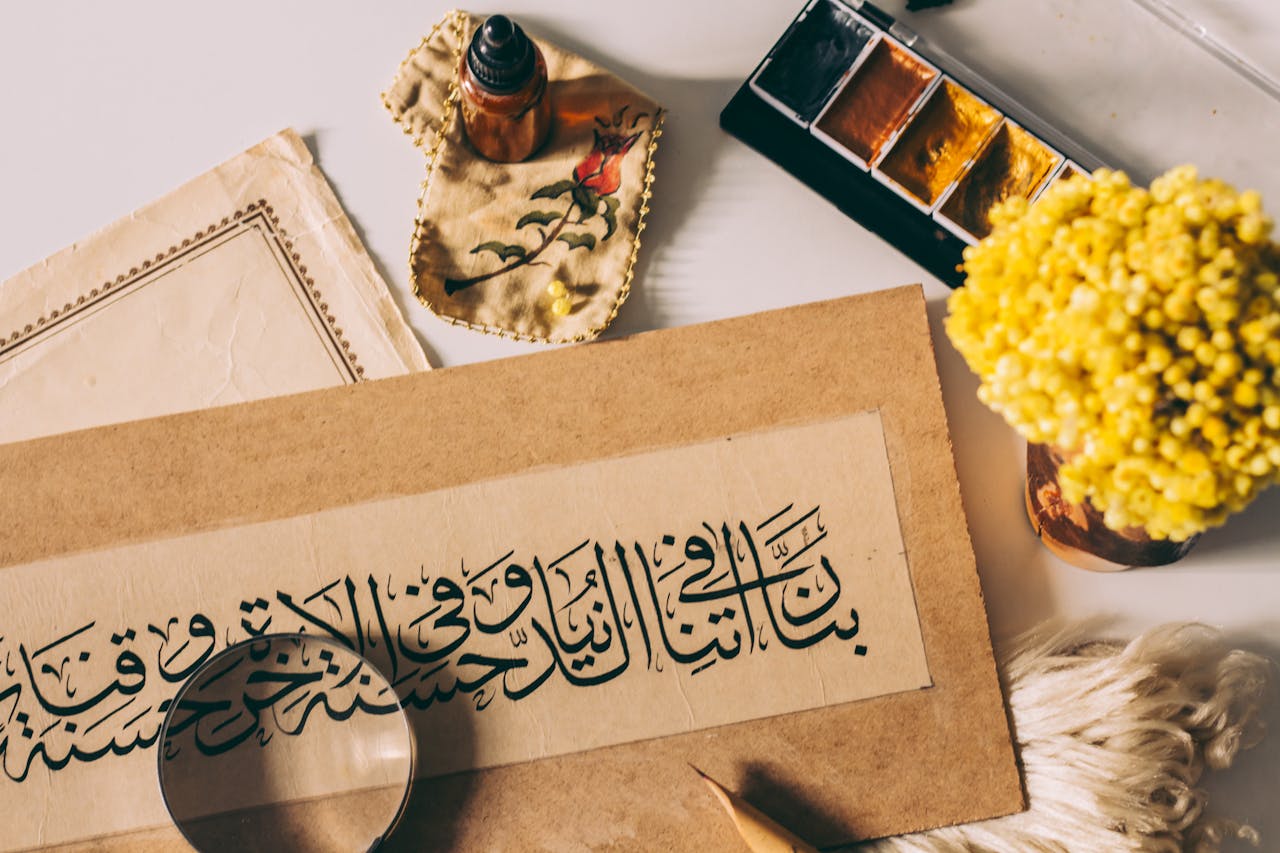 heros-img Flat lay of Arabic calligraphy and artistic tools, highlighting traditional and modern art fusion.